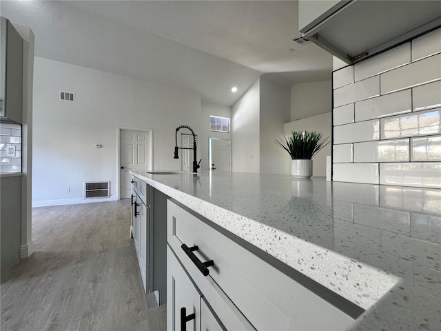 kitchen with high vaulted ceiling, light stone countertops, sink, and light hardwood / wood-style flooring