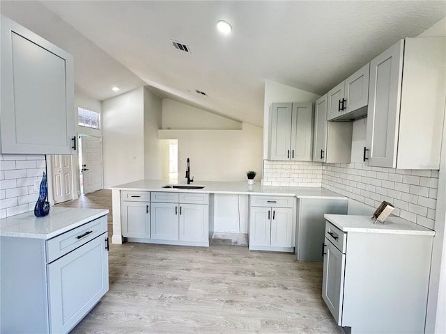 kitchen with sink, light hardwood / wood-style flooring, backsplash, vaulted ceiling, and kitchen peninsula