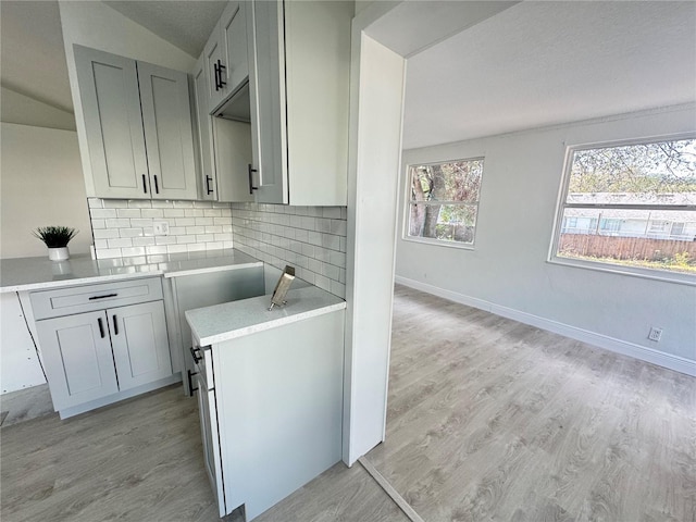 kitchen featuring gray cabinets, vaulted ceiling, decorative backsplash, and light hardwood / wood-style flooring