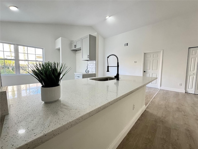 kitchen with hardwood / wood-style flooring, vaulted ceiling, light stone countertops, and sink