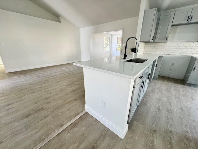 kitchen with gray cabinets, lofted ceiling, sink, decorative backsplash, and light wood-type flooring