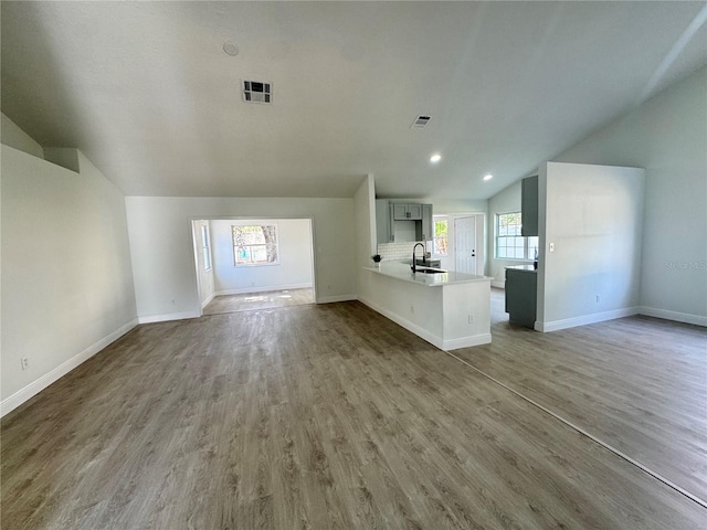 unfurnished living room featuring vaulted ceiling, sink, a wealth of natural light, and dark hardwood / wood-style floors