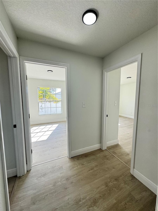 corridor with a textured ceiling and light wood-type flooring