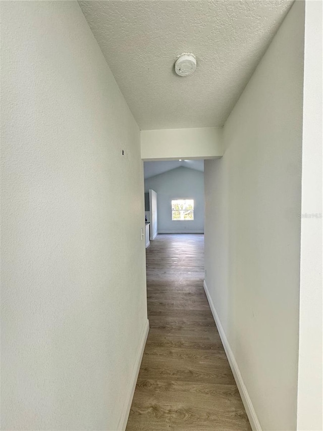 hall featuring wood-type flooring, lofted ceiling, and a textured ceiling