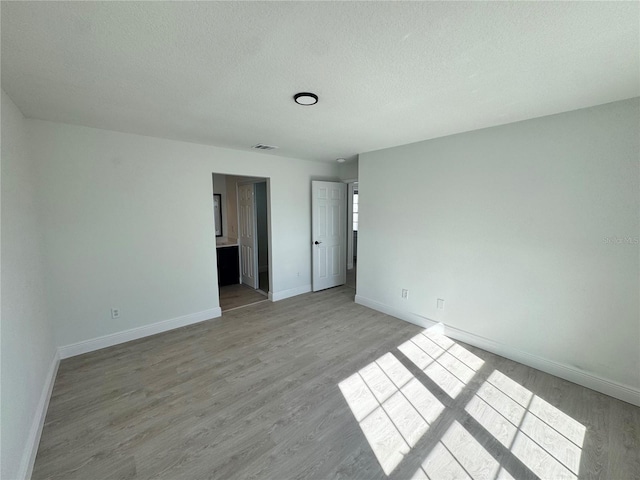 unfurnished bedroom with ensuite bathroom and light hardwood / wood-style flooring