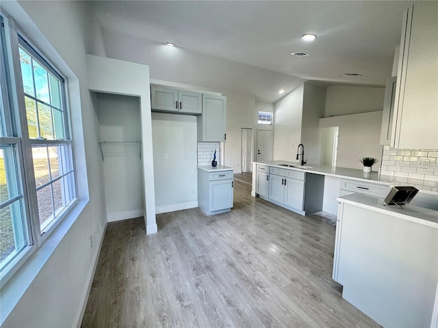 kitchen featuring vaulted ceiling, sink, backsplash, kitchen peninsula, and light wood-type flooring