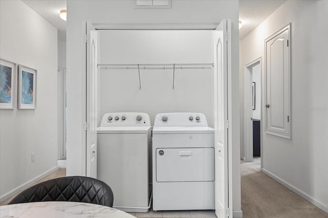 washroom with light colored carpet, a textured ceiling, and washing machine and clothes dryer