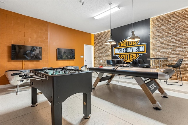 rec room featuring a textured ceiling and brick wall