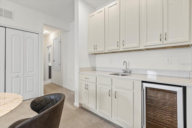 kitchen with white cabinetry, sink, light colored carpet, and beverage cooler