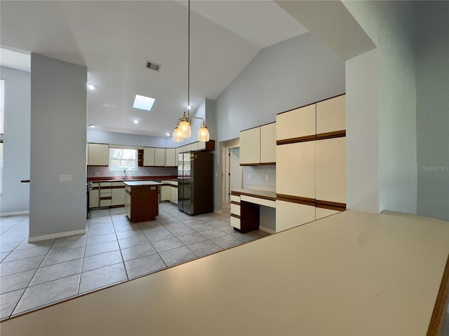 kitchen with cream cabinets, refrigerator, light tile patterned floors, a kitchen island, and decorative light fixtures