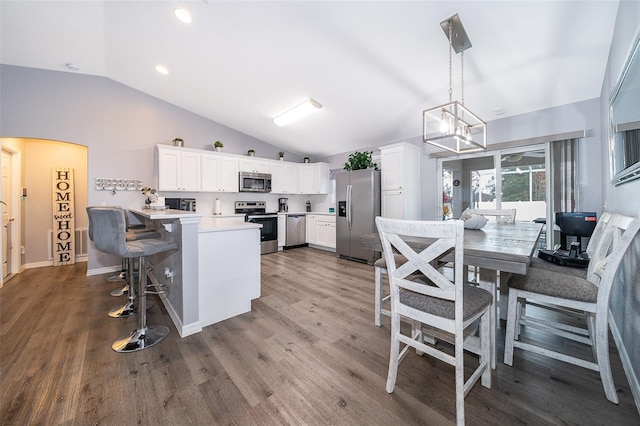 kitchen featuring vaulted ceiling, appliances with stainless steel finishes, decorative light fixtures, white cabinets, and kitchen peninsula