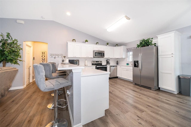 kitchen with a breakfast bar, appliances with stainless steel finishes, white cabinets, vaulted ceiling, and light wood-type flooring