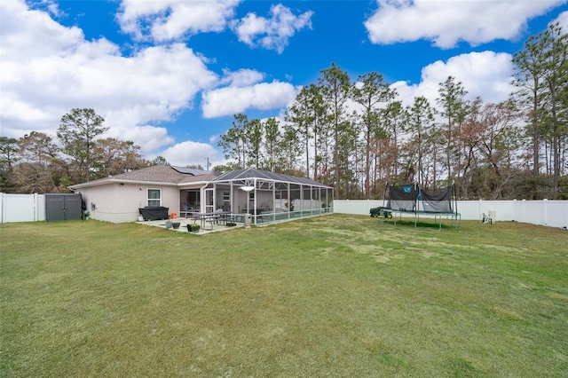 rear view of house with a trampoline, a yard, glass enclosure, and a patio