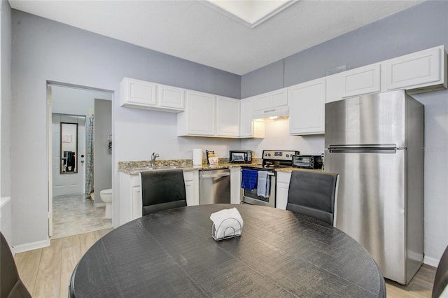 kitchen with white cabinets, light hardwood / wood-style floors, light stone countertops, and stainless steel appliances