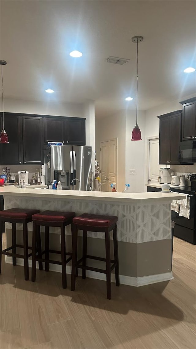 kitchen with black appliances, hanging light fixtures, light hardwood / wood-style floors, and a kitchen breakfast bar