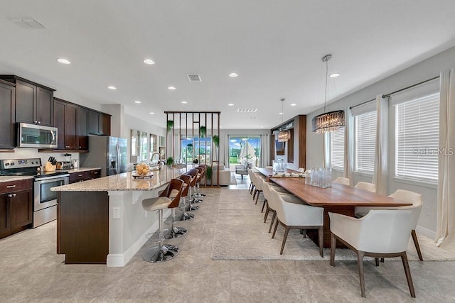 kitchen featuring a breakfast bar, hanging light fixtures, light stone countertops, appliances with stainless steel finishes, and an island with sink