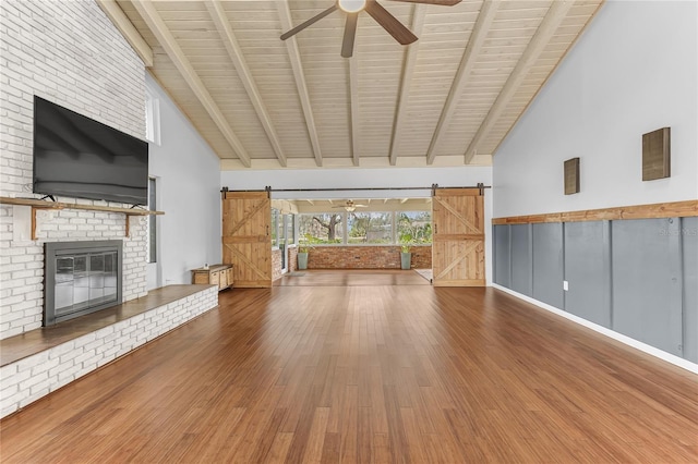 unfurnished living room with high vaulted ceiling, wood-type flooring, beam ceiling, and a barn door