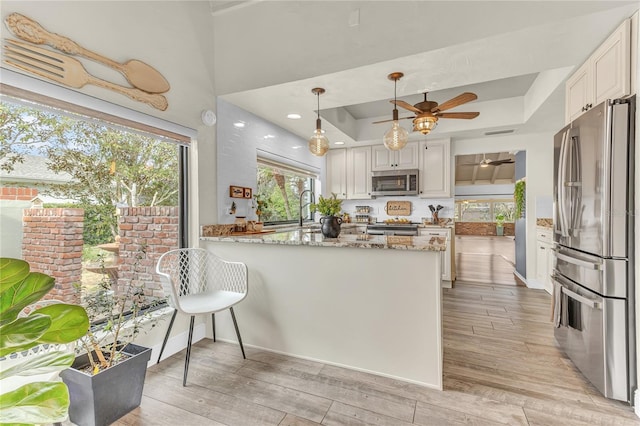 kitchen featuring appliances with stainless steel finishes, white cabinets, kitchen peninsula, light stone counters, and a tray ceiling