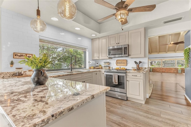 kitchen with light stone countertops, hanging light fixtures, sink, light wood-type flooring, and stainless steel appliances