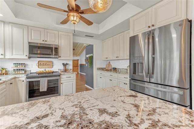 kitchen with backsplash, a raised ceiling, appliances with stainless steel finishes, and light stone counters