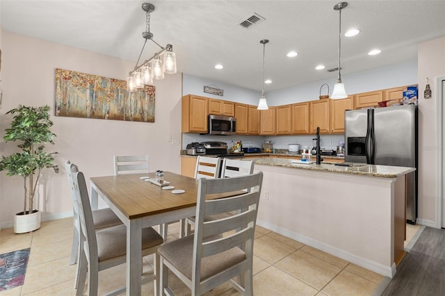 kitchen with stainless steel appliances, hanging light fixtures, light tile patterned floors, and an island with sink