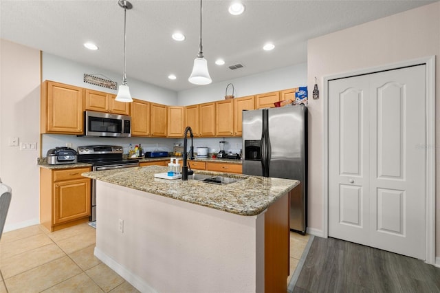 kitchen featuring appliances with stainless steel finishes, hanging light fixtures, sink, light stone counters, and a center island with sink