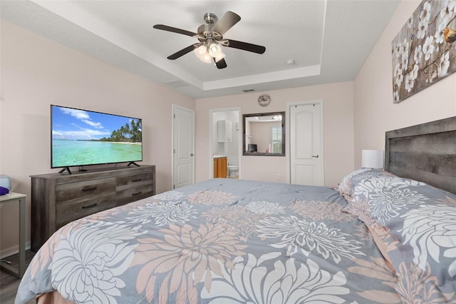 bedroom with ceiling fan, a textured ceiling, connected bathroom, and a tray ceiling