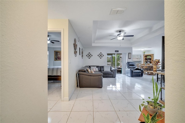 living room featuring ceiling fan and a raised ceiling