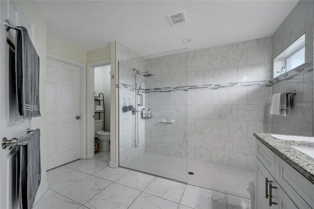 bathroom featuring toilet, tiled shower, and vanity