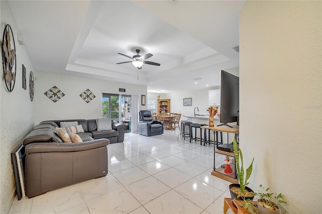 living room with ceiling fan and a tray ceiling