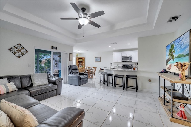 living room with ceiling fan, sink, and a tray ceiling