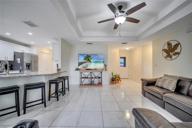 living room with a raised ceiling and ceiling fan