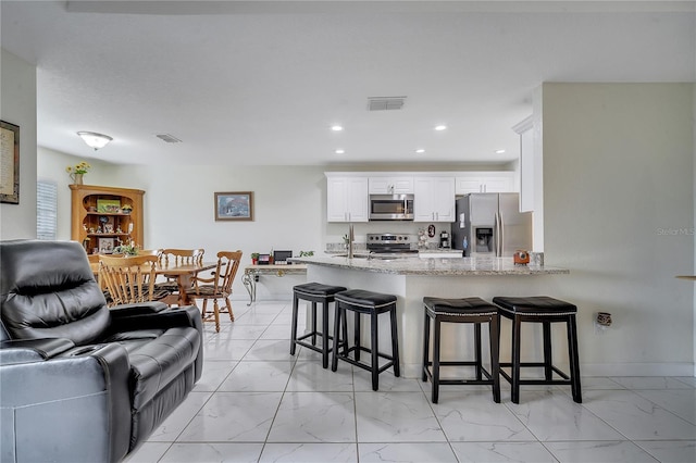 kitchen with kitchen peninsula, white cabinetry, light stone countertops, appliances with stainless steel finishes, and a kitchen breakfast bar