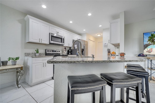 kitchen featuring appliances with stainless steel finishes, a kitchen bar, white cabinets, and light stone counters