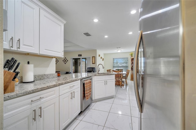 kitchen with light stone countertops, appliances with stainless steel finishes, white cabinetry, sink, and kitchen peninsula