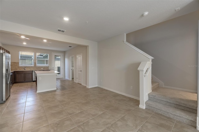 kitchen with sink, light tile patterned floors, a center island, stainless steel refrigerator with ice dispenser, and tasteful backsplash