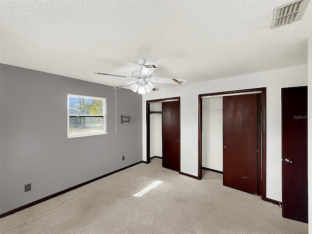 unfurnished bedroom with multiple closets, light colored carpet, a textured ceiling, and ceiling fan