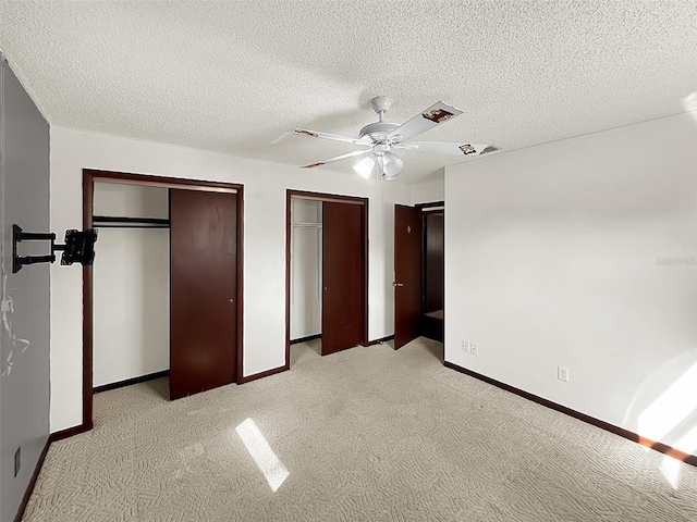 unfurnished bedroom with multiple closets, light carpet, a textured ceiling, and ceiling fan