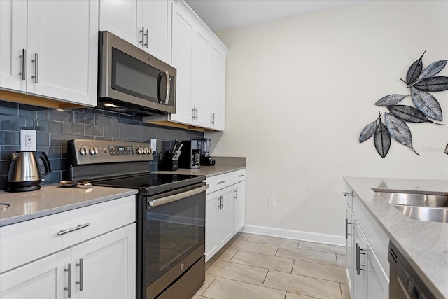 kitchen with appliances with stainless steel finishes, tasteful backsplash, white cabinetry, sink, and light stone countertops