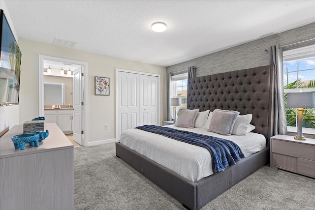 bedroom with light colored carpet, connected bathroom, a closet, and a textured ceiling