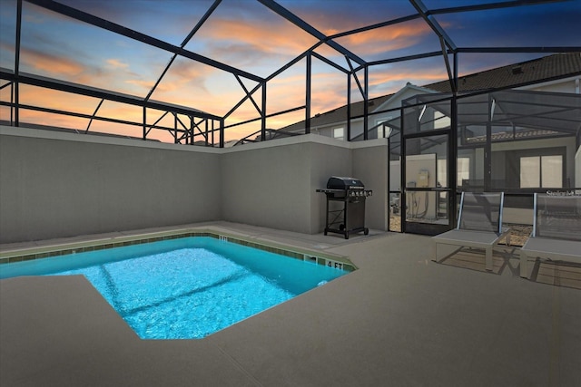 pool at dusk with area for grilling, a patio area, and glass enclosure