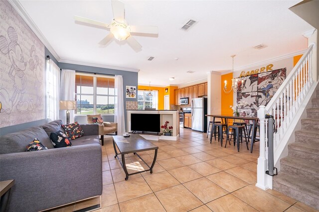 living area with stairs, visible vents, ornamental molding, light tile patterned flooring, and ceiling fan with notable chandelier