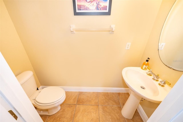 half bath with tile patterned flooring, baseboards, a sink, and toilet