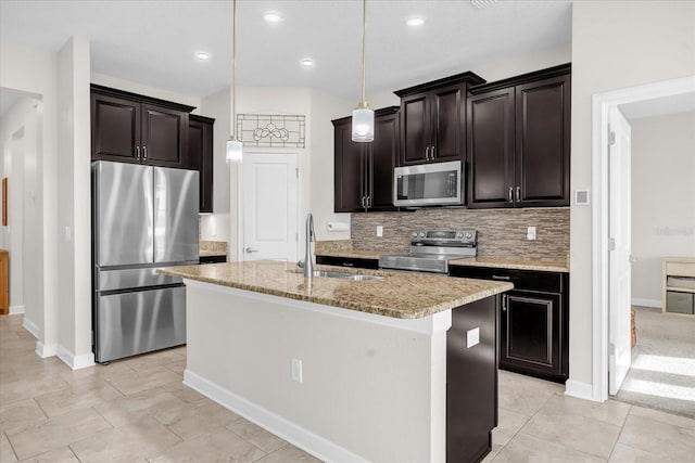 kitchen with appliances with stainless steel finishes, decorative light fixtures, sink, light stone counters, and a kitchen island with sink