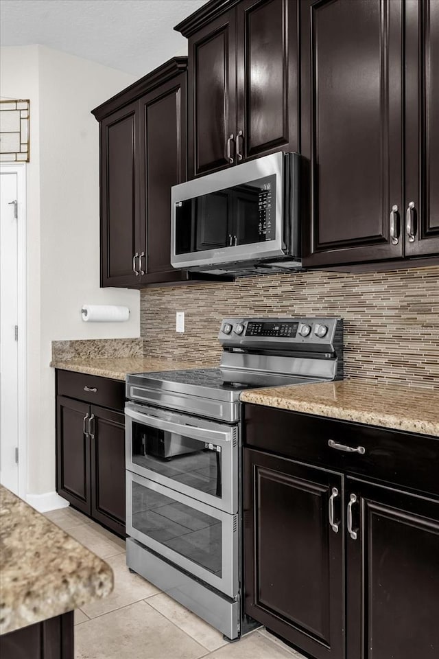 kitchen with light tile patterned floors, decorative backsplash, dark brown cabinets, stainless steel appliances, and light stone counters