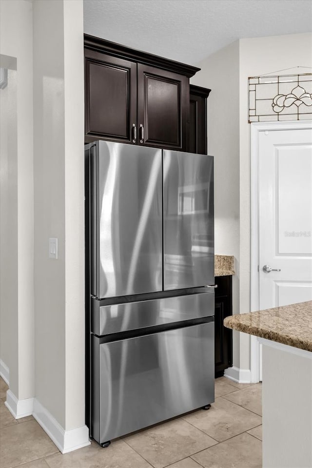 kitchen featuring dark brown cabinetry, light stone counters, light tile patterned floors, and stainless steel fridge