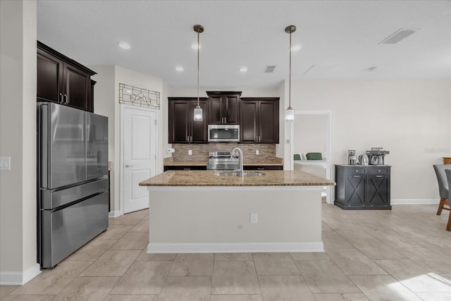 kitchen featuring hanging light fixtures, appliances with stainless steel finishes, sink, light stone countertops, and an island with sink