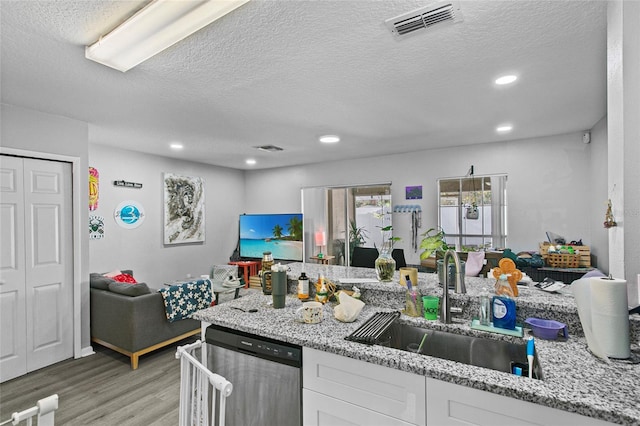 kitchen featuring light stone countertops, a textured ceiling, white cabinetry, stainless steel dishwasher, and sink