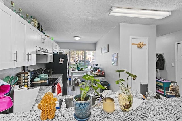 kitchen with a textured ceiling, white cabinets, black fridge, light stone counters, and range with electric stovetop