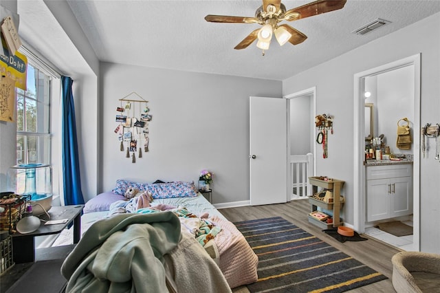 bedroom with ceiling fan, ensuite bathroom, a textured ceiling, and wood-type flooring